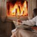 a woman sitting in front of a fireplace holding a glass of wine