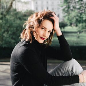 smiling woman touching hair on fence against park