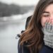 woman in black hooded down jacket covering her face with grey fingerless gloves