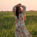 young woman with raised arms standing in flower field and smiling