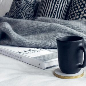 black ceramic mug on round white and beige coaster on white textile beside book